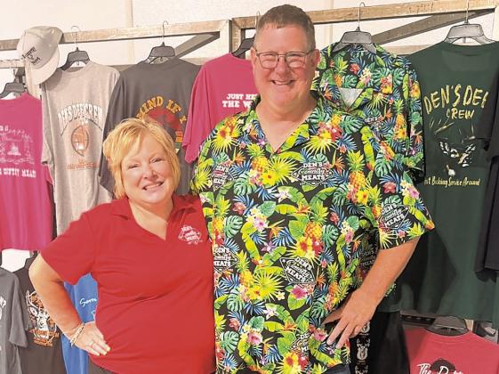 Proprietors Kim &amp;amp; Dennis Schaardt in front of a display of Den’s Country Meats t-shirts. Given some hints about how to do something “besides just stand there,” Kim Schaardt asks, “So you want some sass?!” Dennis, he’s not sassy, he’s just pleased and delighted to be in the business for so long and still going strong.