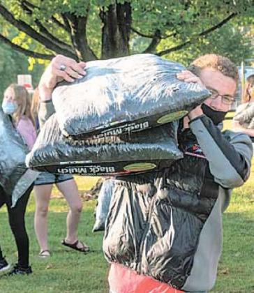 Jacob Lytle carries sacks of Black Mulch, left is Taegan Rottman and right is Hallye Friedly.