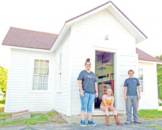 Historical Society volunteers Larissa Weimers, Colby Hedden, &amp;amp; Zack Hedden stand at the door of the Maple Wood Country School Museum in Table Rock. The school originally sat near the intersection of what became Highways 50 &amp;amp; 65. It was built in 1874, almost 20 years after Lydia Griffing taught 11 students in her 11 x 13’ log cabin.