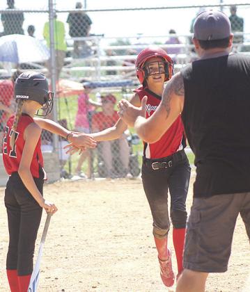 Pictured at right: P.C.’s Sophia Sunneberg (center) gets congratulated on stealing home by teammate Vanessa Gottula (#27) and Coach Mark Sunneberg (at right). Pictured below right: P.C.’s Amelia Strathman takes a swing at a ball during the game against Weeping Water. photos by Paula Jasa/Republican