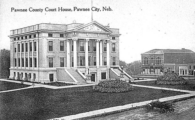 The new courthouse, finished in 1912. Victorian flower beds flank the front entrance. The Pawnee City Opera House looms in the background.