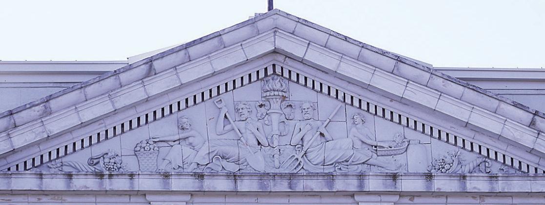 The pediment above the colossal Corinthian columns of the north portico. “Dentils” (small repeating blocks for ornamentation) run above and below it, “Triglyphs” (the four small blocks with grooves) anchor the triangular gable, and within the triangle is a terra cotta sculpture with interesting figures.