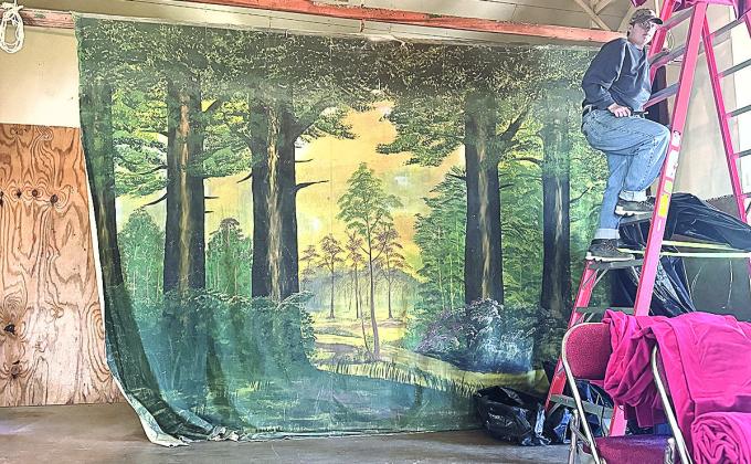 The forest scene of the far back curtain, carpenter’s assistant Toby Evans at the ladder during the project of hanging the new stage curtains.