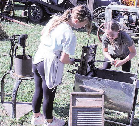 Student Kennedy pulls a t-shirt through a ringer as student Paisley cranks the handle