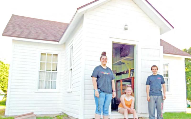 Historical Society volunteers Larissa Weimers, Colby Hedden, &amp;amp; Zack Hedden stand at the door of the Maple Wood Country School Museum in Table Rock. The school originally sat near the intersection of what became Highways 50 &amp;amp; 65. It was built in 1874, almost 20 years after Lydia Griffing taught 11 students in her 11 x 13’ log cabin.