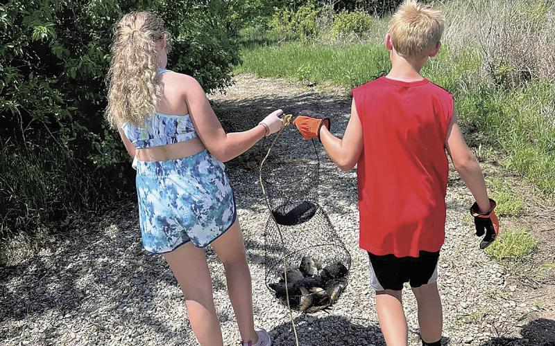 Siblings Aubrey (left) and Noah Marr (right) carry a net of fish down a gravel path