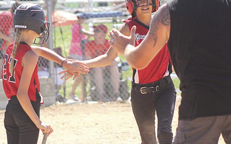 Pictured at right: P.C.’s Sophia Sunneberg (center) gets congratulated on stealing home by teammate Vanessa Gottula (#27) and Coach Mark Sunneberg (at right). Pictured below right: P.C.’s Amelia Strathman takes a swing at a ball during the game against Weeping Water. photos by Paula Jasa/Republican