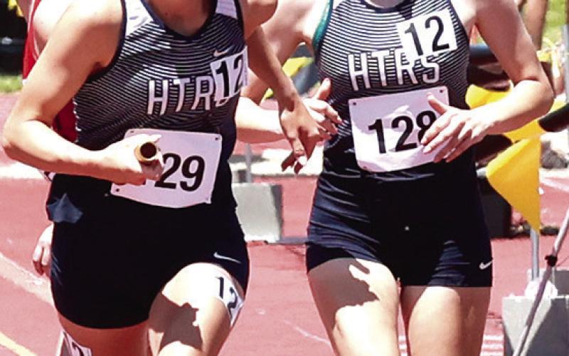 HTRS Girls’ 3200 M. Relay team of Grayson Sherman (photo left) and Lillian Bowen (photo right) taking the baton from Addi Bittner (far right) ran the first race of the 2024 Class D State Track Meet. Photos courtesy of Lorrie Novak