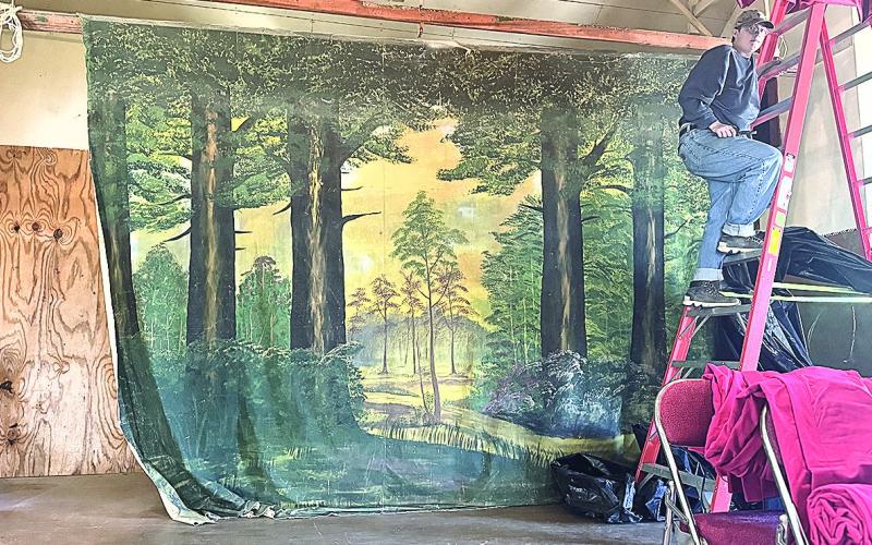 The forest scene of the far back curtain, carpenter’s assistant Toby Evans at the ladder during the project of hanging the new stage curtains.