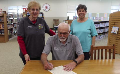 Pawnee City Mayor Charlie Hatfield (center) signs a proclamation designating April 19-25 as National Library Week. Library Director Lola Seitz (left) and Library Board President Patti Rice (right) flank him.