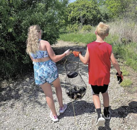 Siblings Aubrey (left) and Noah Marr (right) carry a net of fish down a gravel path