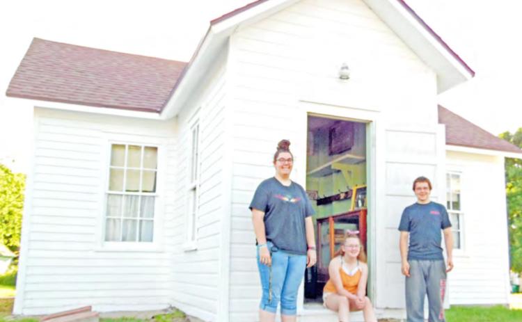 Historical Society volunteers Larissa Weimers, Colby Hedden, &amp; Zack Hedden stand at the door of the Maple Wood Country School Museum in Table Rock. The school originally sat near the intersection of what became Highways 50 &amp; 65. It was built in 1874, almost 20 years after Lydia Griffing taught 11 students in her 11 x 13’ log cabin.