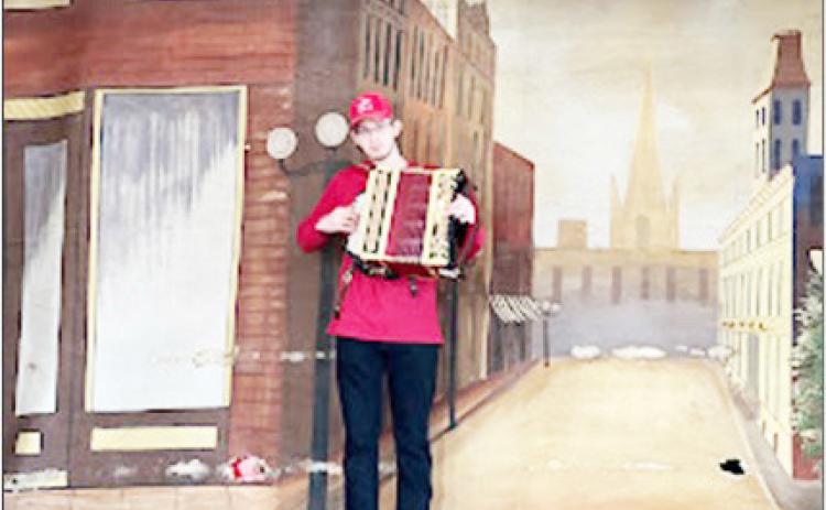 Trey Blecha in December 2021 at the ZCBJ Hall, Du Bois. It was a Polka Christmas concert featuring the Czechlanders Orchestra that also celebrated the 100th anniversary of the hall, sponsored by the Pawnee County Arts Council &amp; the Pawnee County Promotional Network (PCPN). Coinciding with that, PCPN re-hung the original painted canvas curtains. Here, Trey stands before the mid-stage curtain, which bears a street scene from old Prague.