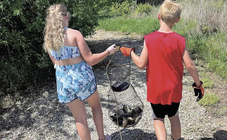 Siblings Aubrey (left) and Noah Marr (right) carry a net of fish down a gravel path